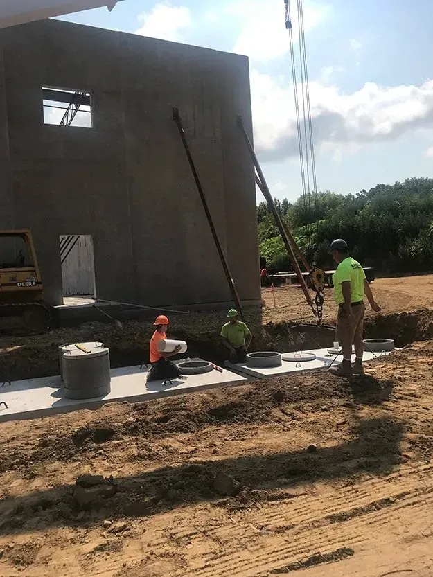 Workers laying concrete outside an unfinished building on a muddy construction site