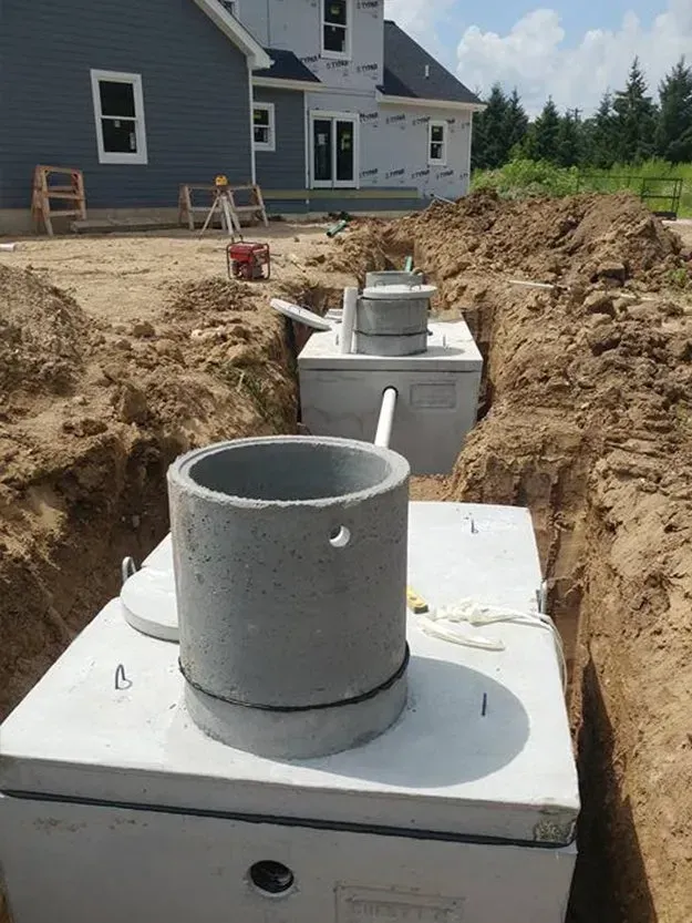 Septic system tanks and risers in a trench beside a house under construction