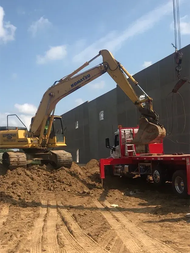 Yellow excavator loading dirt into a red dump truck at a construction site