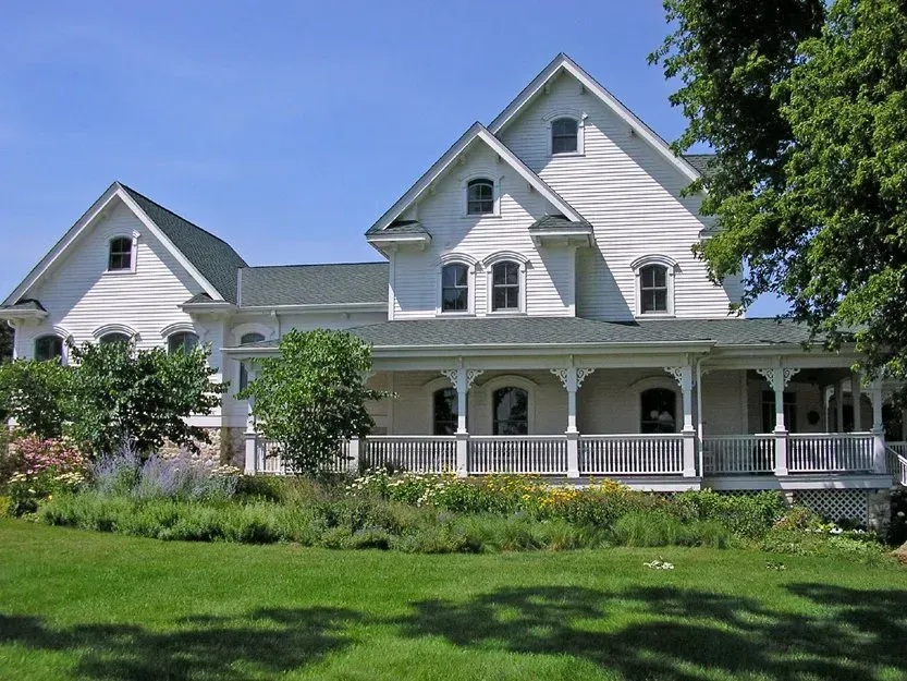 White Victorian house with a wraparound porch and green lawn under sunny sky