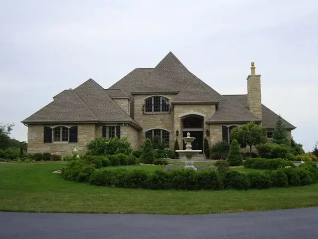 Large beige suburban house with a peaked roof and manicured front lawn