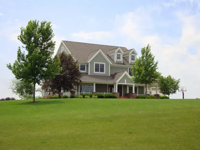 Gray house with a front porch on a green lawn under a partly cloudy sky