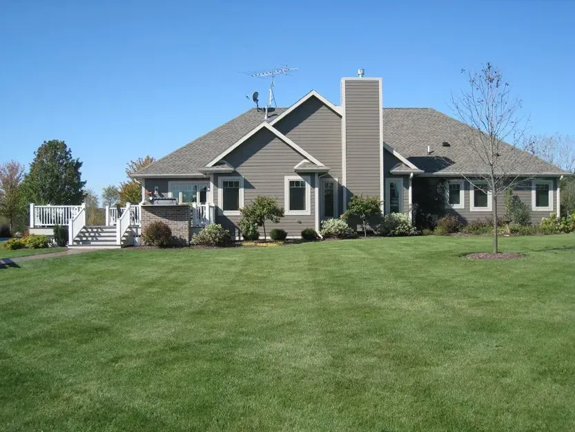 Single-story suburban house with a large green lawn under a clear blue sky