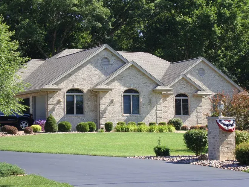 Stone suburban house with gray roof, manicured lawn, and a patriotic mailbox at the curb