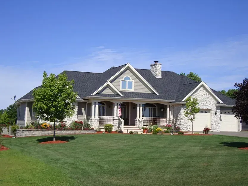 Large suburban house with gray roof, white siding, and a green lawn under a clear blue sky
