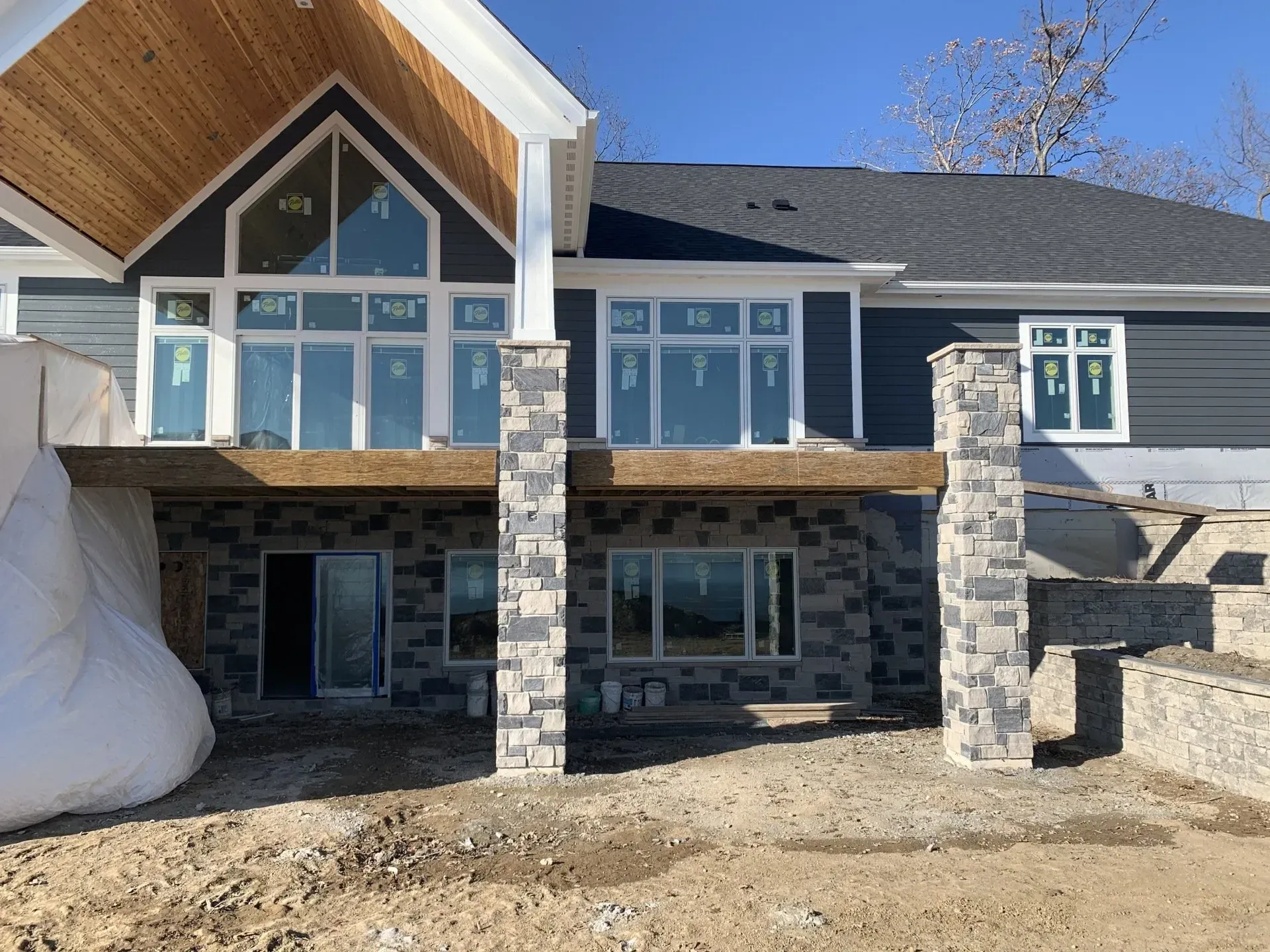 New house exterior with stone columns, large windows, and unfinished landscaping