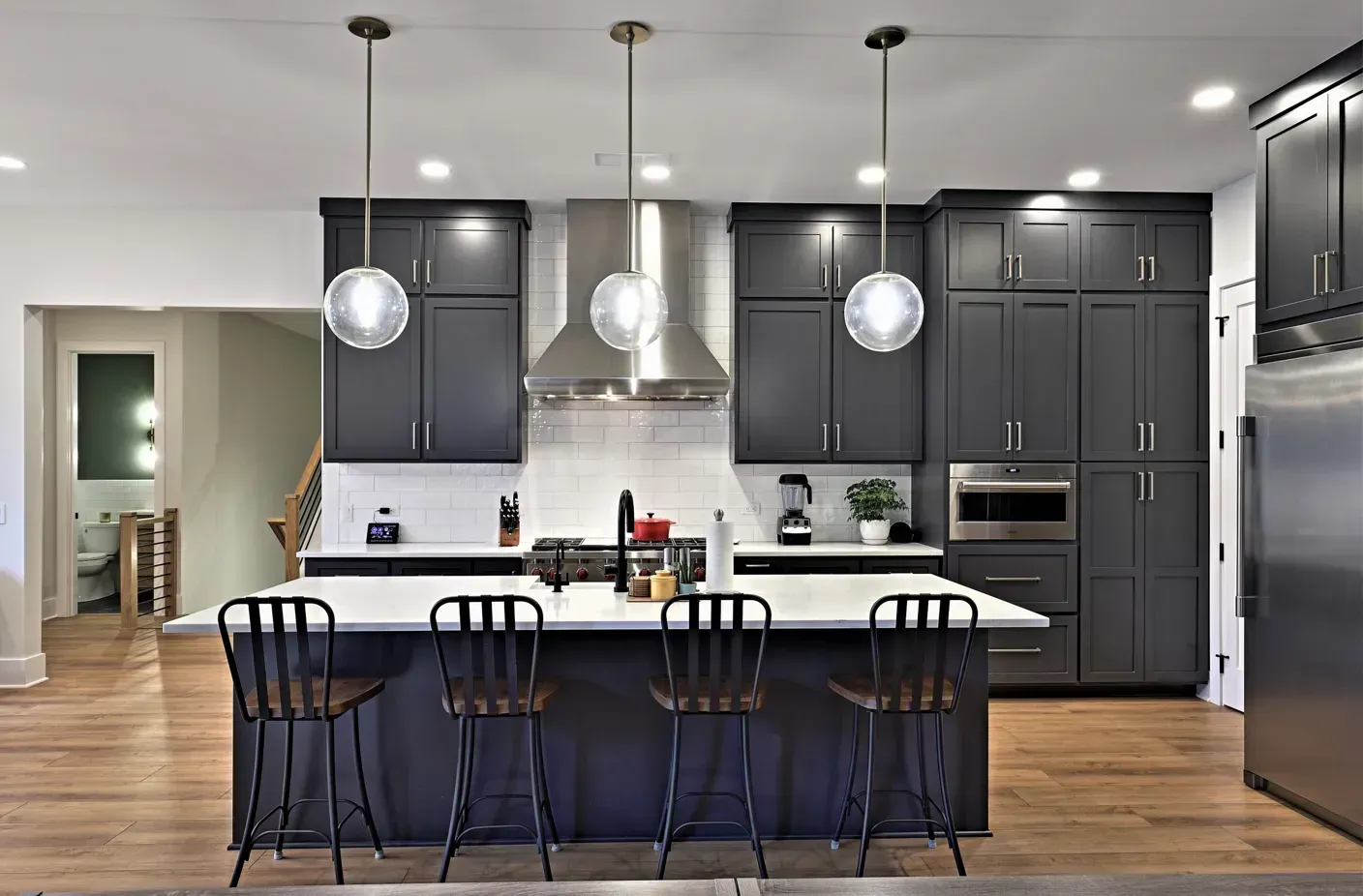 Modern kitchen with dark cabinets, white island, pendant lights, and four blue barstools