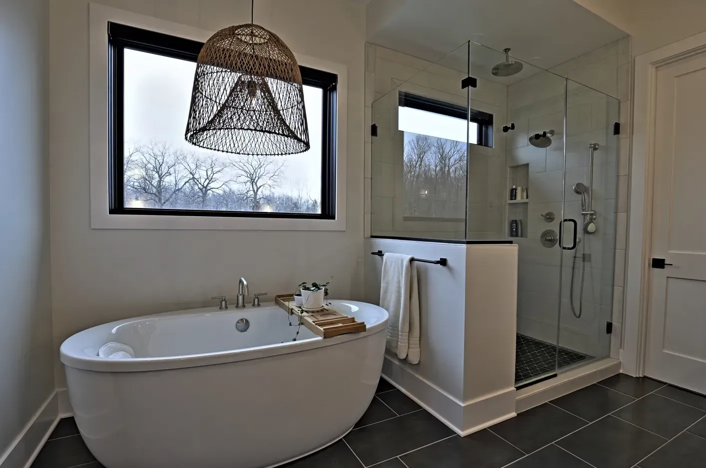 Modern bathroom with freestanding tub, glass shower, large window, and dark tile floor