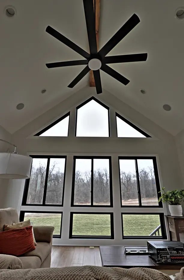 Bright living room with high vaulted ceiling, large fan, and wall of windows overlooking a grassy yard