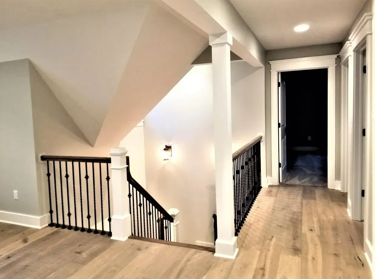 Upper hallway with wood floors, black stair railing, white walls, and a hallway leading into a dark room