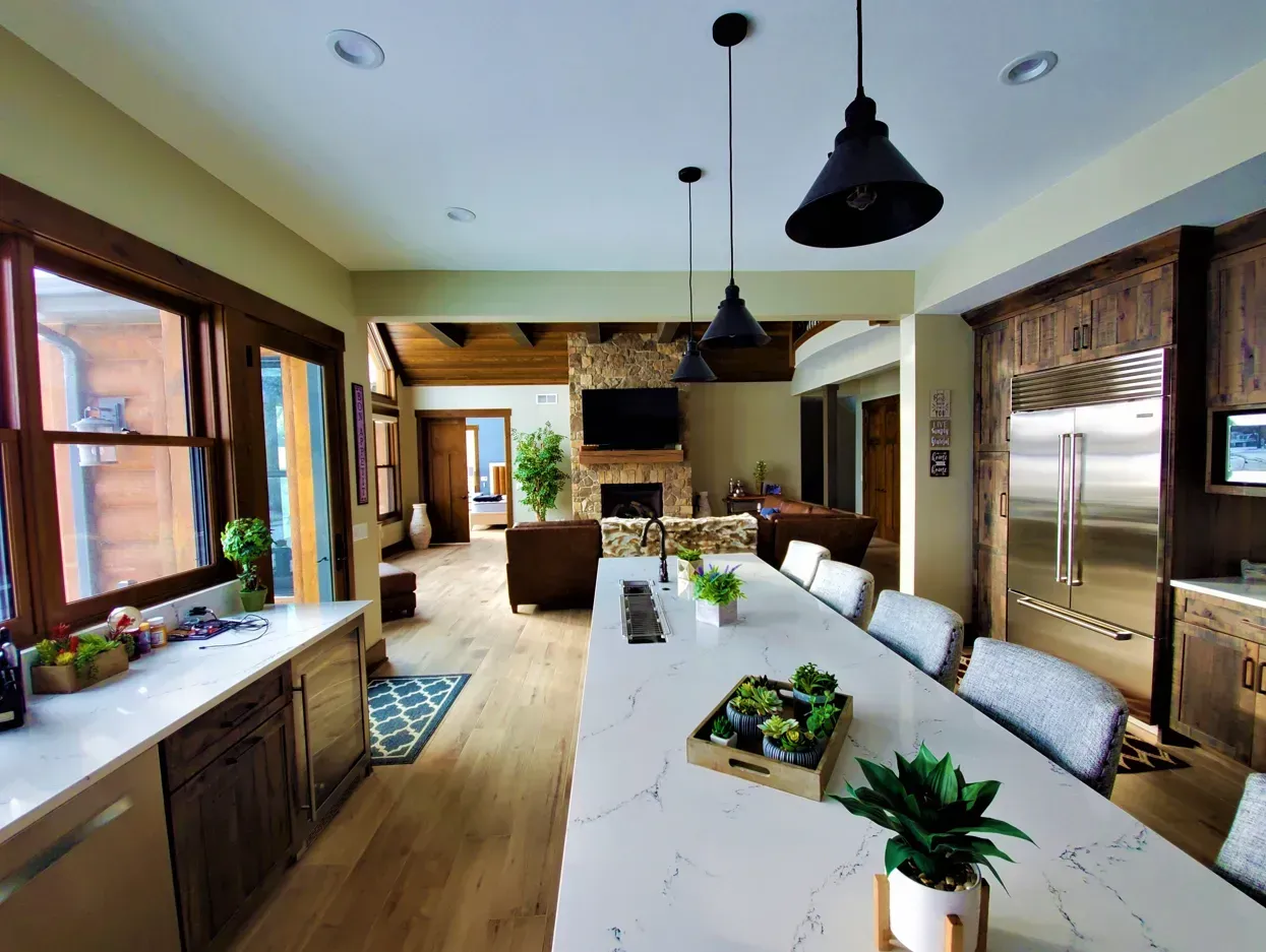 Bright modern kitchen and dining area with white island, black pendant lights, and wood floors