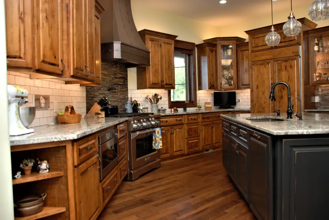Wooden kitchen with granite island, black appliances, and warm lighting