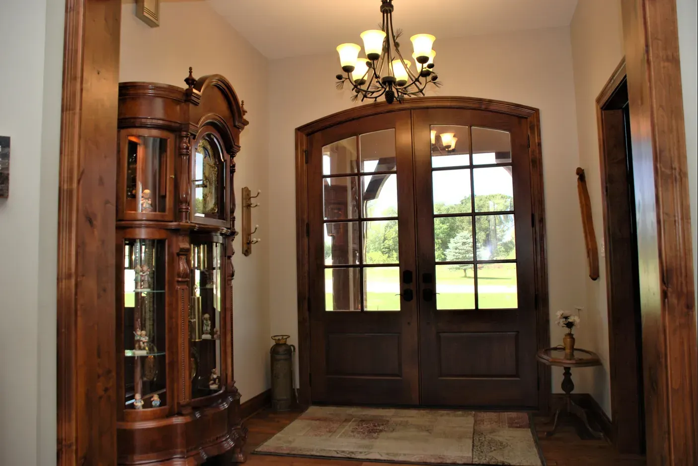 Elegant foyer with carved wooden cabinets, double front doors, chandelier, and rug.