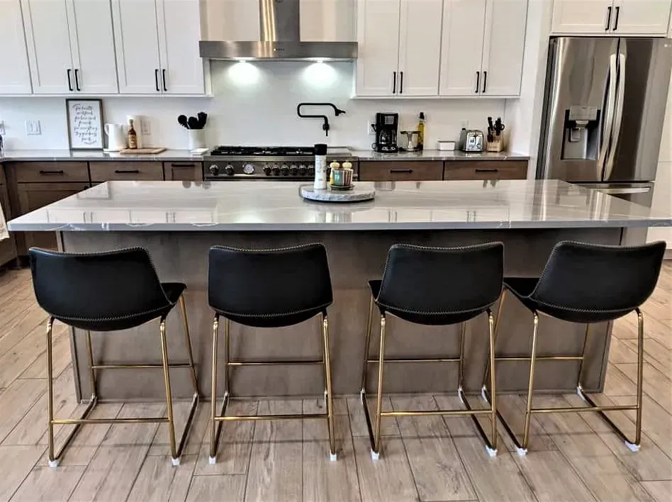 Modern kitchen with white cabinets, stainless steel appliances, and four black bar stools at a large island