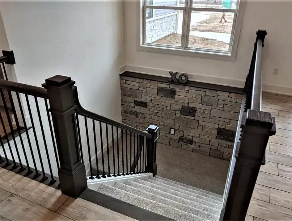 Stairway with dark railings, beige tile floor, and a window above a stone accent wall.