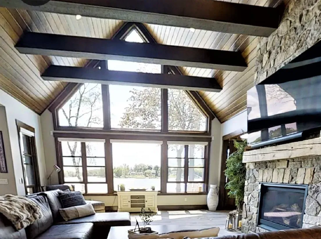 Cozy living room with stone fireplace, exposed beams, large windows, and mountain views