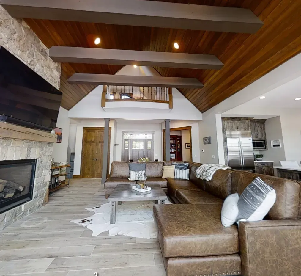 Modern living room with vaulted wood ceiling, stone fireplace, leather sectional, and open kitchen area