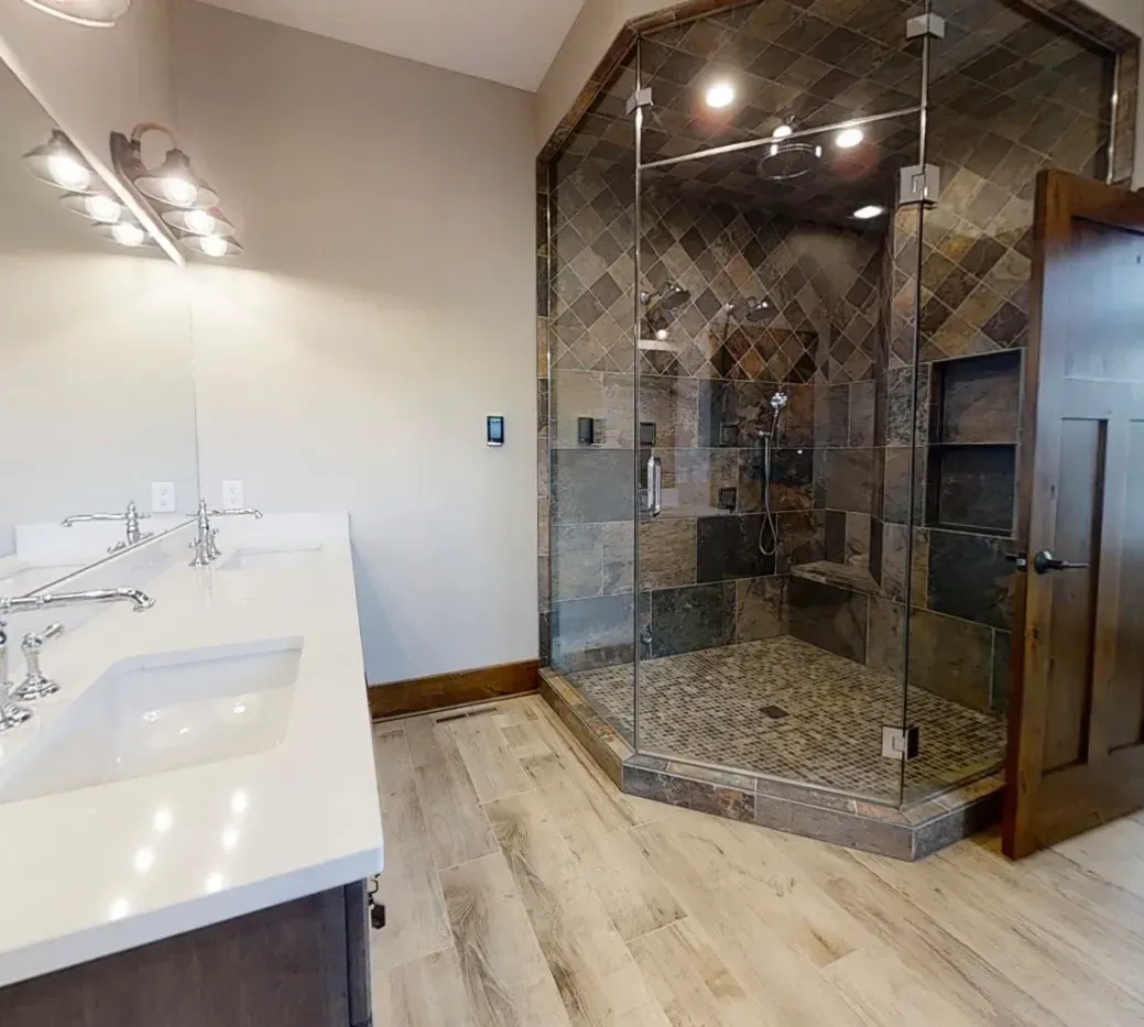 Modern bathroom with white vanity, mirror lights, and a large dark tiled glass shower enclosure