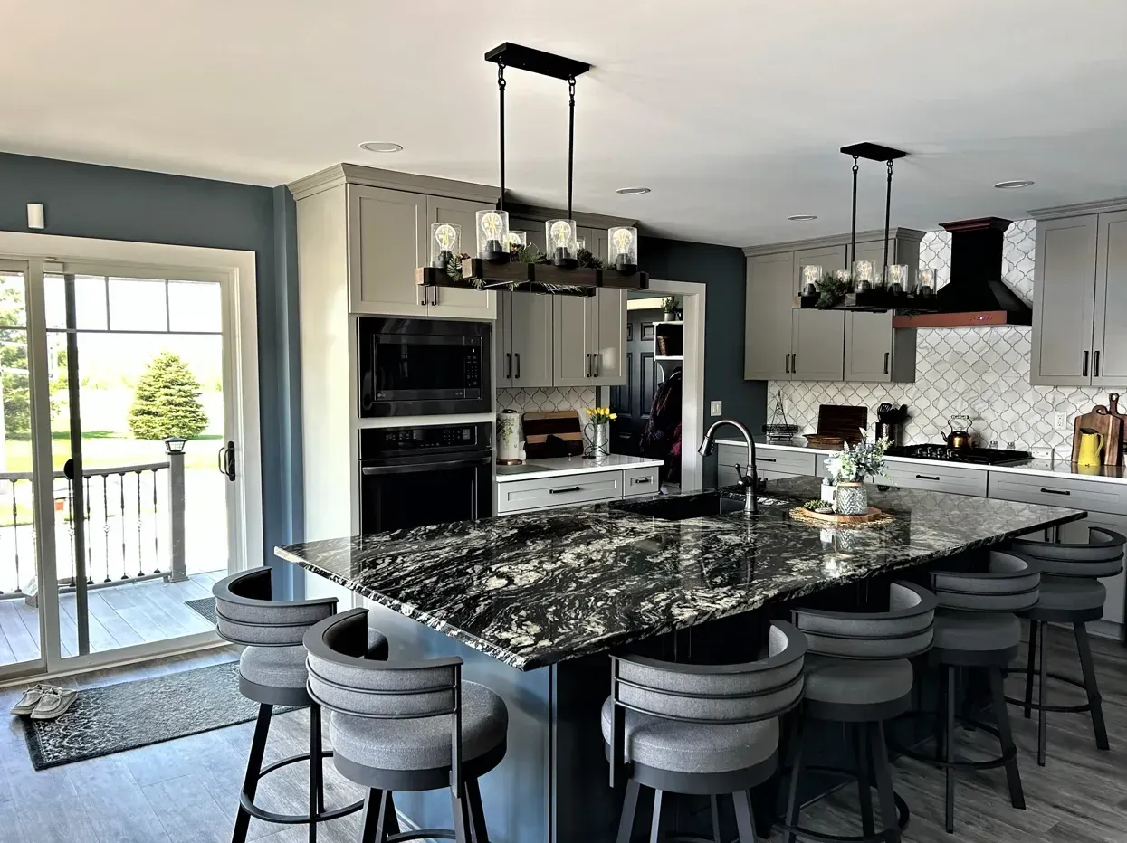 Modern kitchen with large granite island, barstools, pendant lights, and sliding glass doors to a patio