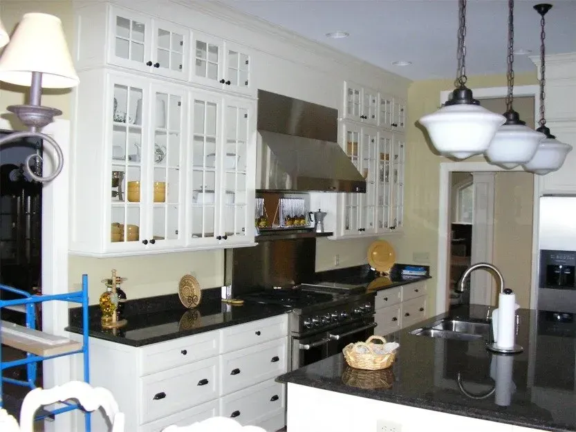 Modern white kitchen with black countertops, stainless steel appliances, and pendant lights over an island