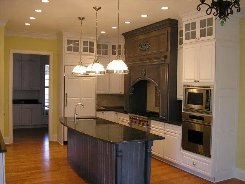 Modern kitchen with dark island, white cabinets, built-in ovens, and hanging pendant lights