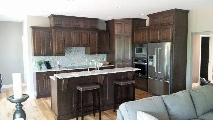 Modern kitchen with dark wood cabinets, marble island, stainless fridge, and two bar stools