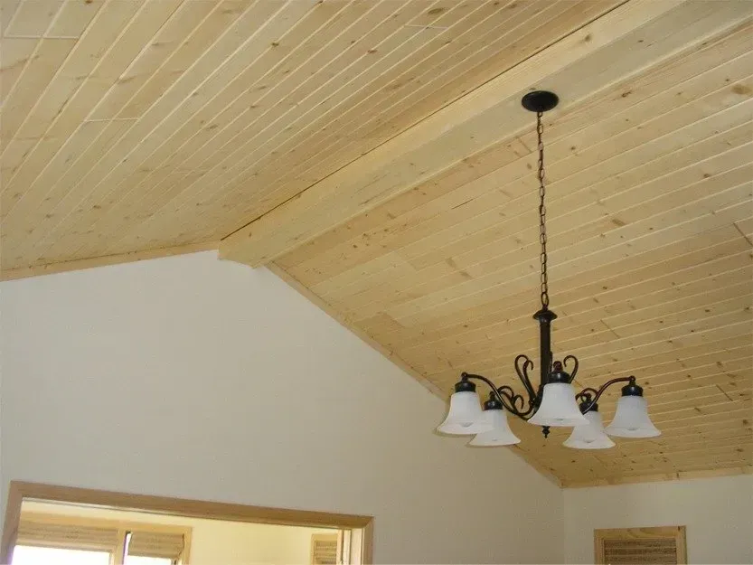 Chandelier hanging from a vaulted wood-paneled ceiling above a bright room.