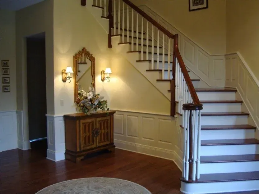 Foyer with curved staircase, dark wood floor, and ornate console table with mirror and wall sconces