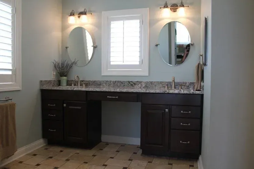 Bathroom vanity with double sinks, granite countertop, dark cabinets, and round mirrors above.