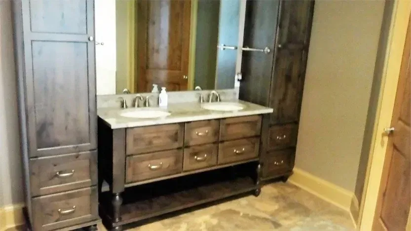 Bathroom vanity with double sinks, mirror, and dark wood cabinets against beige walls.