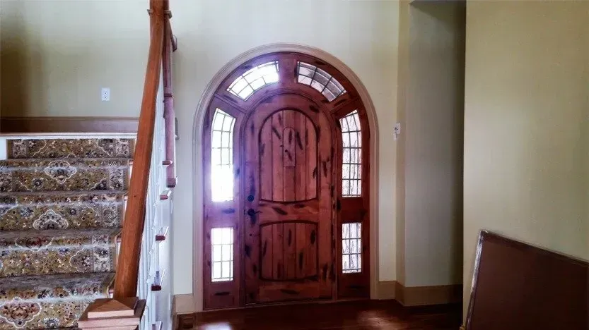 Front entryway with a wooden arched door, sidelights, and staircase on the left