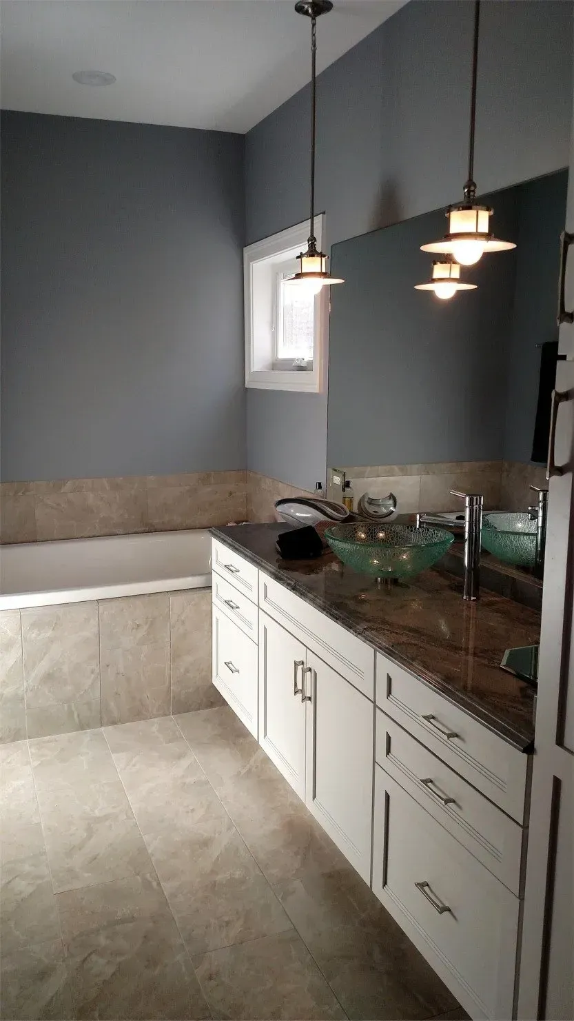 Modern kitchen with gray walls, white cabinets, granite countertop, sink, and pendant lights