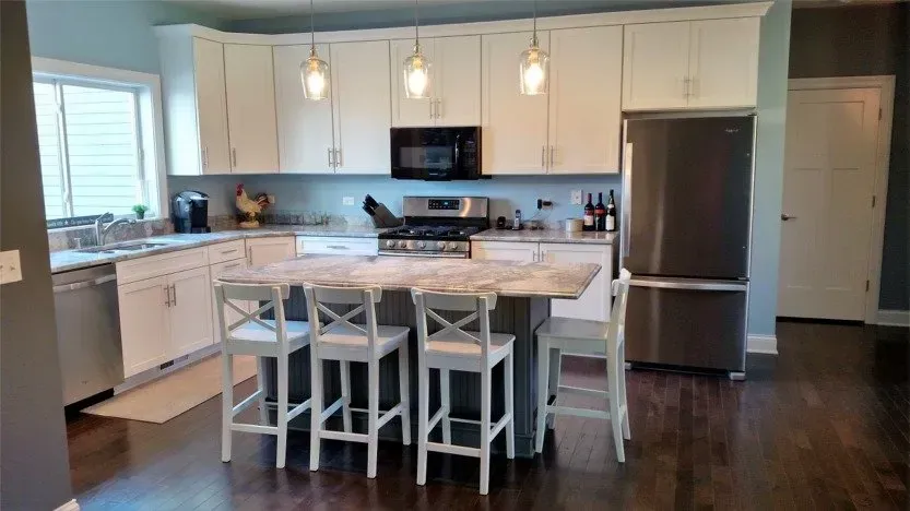 Modern kitchen with white cabinets, marble island, bar stools, and stainless steel appliances