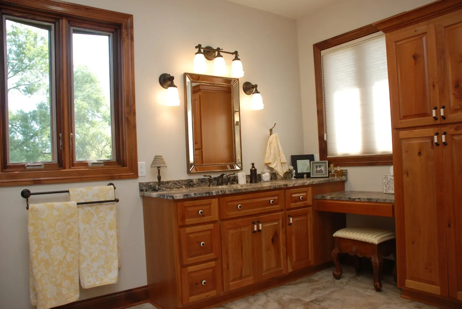 Warm bathroom with wood cabinets, granite vanity, mirror, window, and towel rack