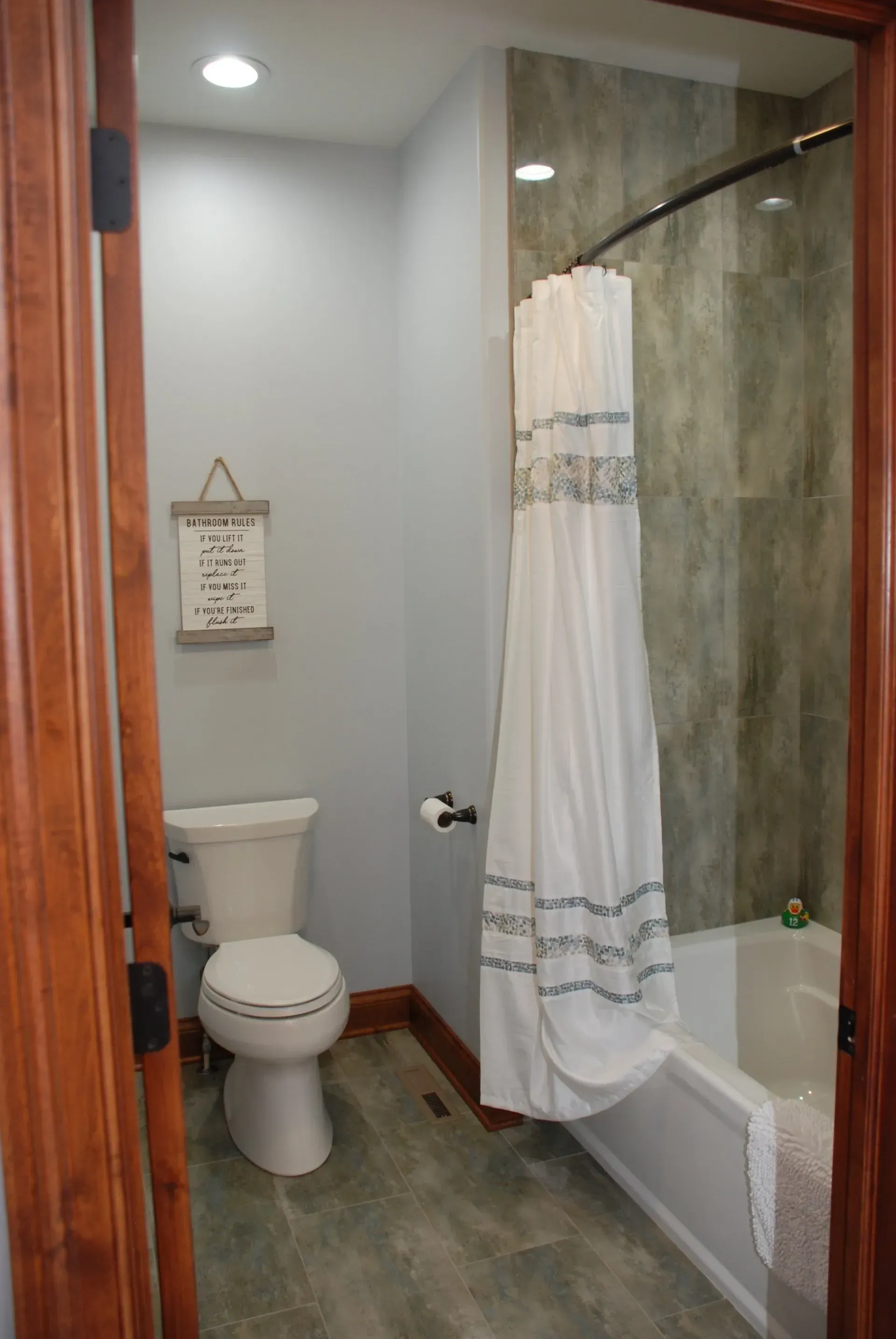 Small bathroom with toilet, glass shower, and white shower curtain beside a wooden door.