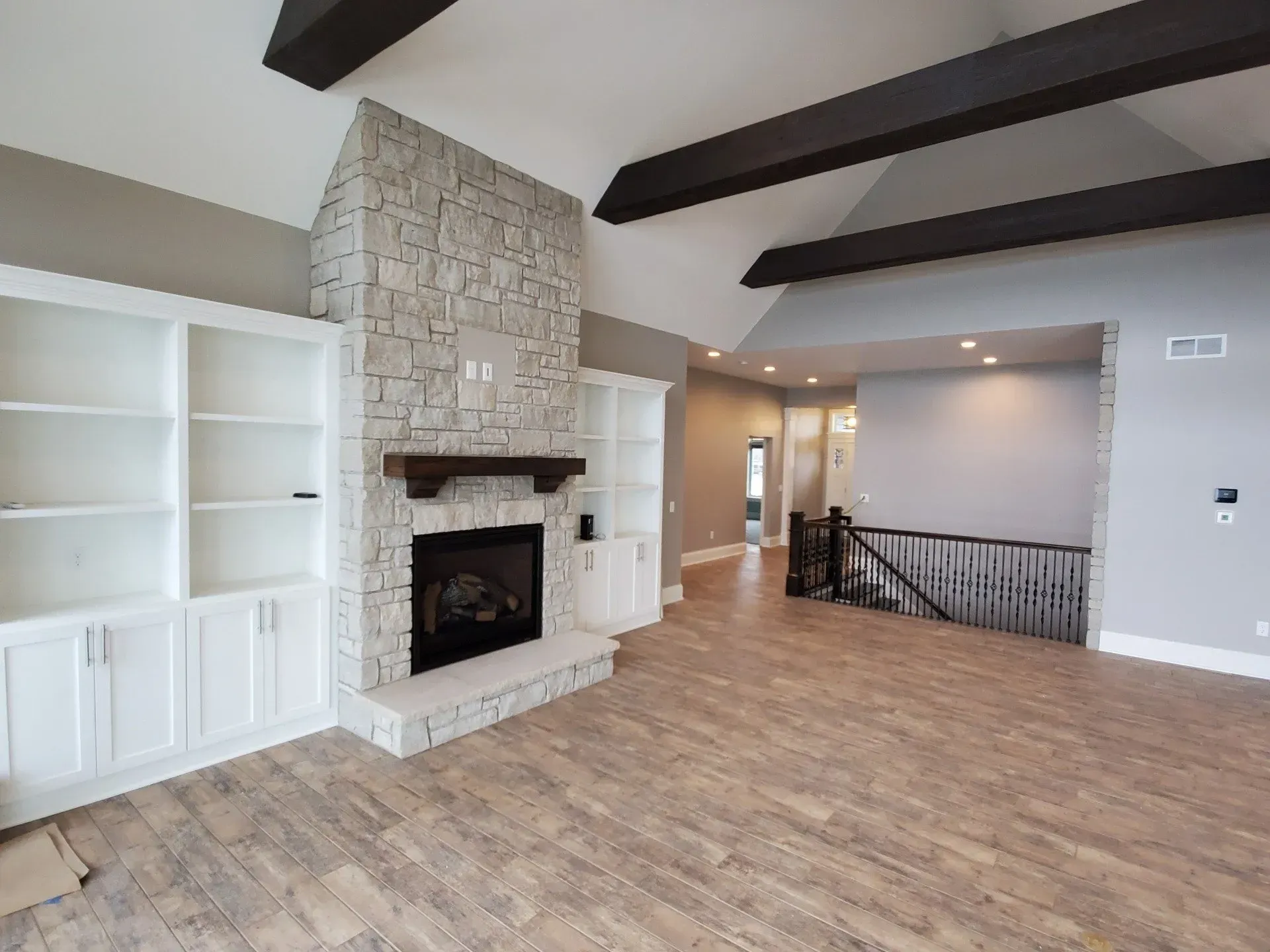 Empty living room with stone fireplace, exposed dark beams, and light wood flooring