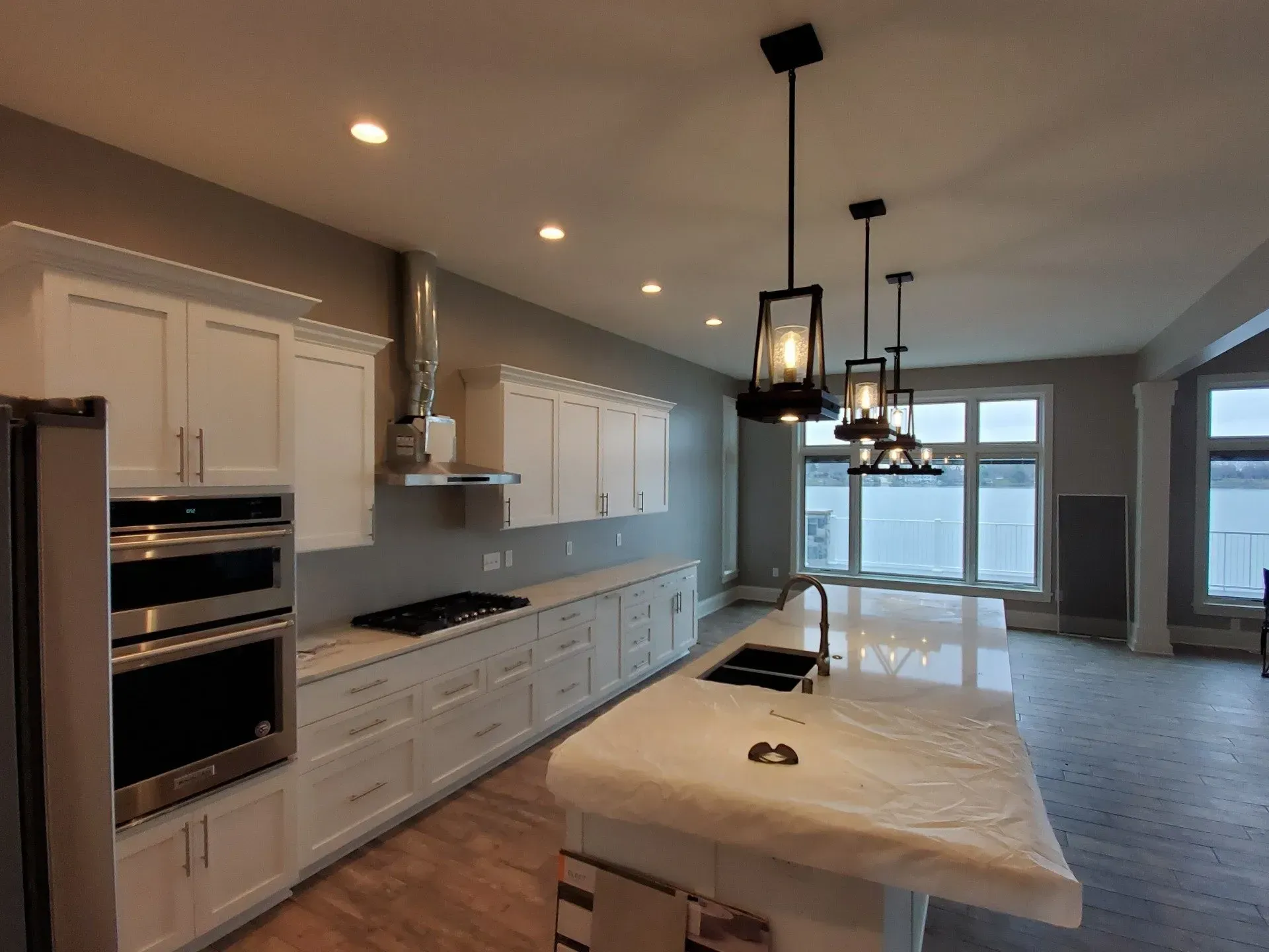 Bright modern kitchen with white cabinets, island, pendant lights, and large windows overlooking water