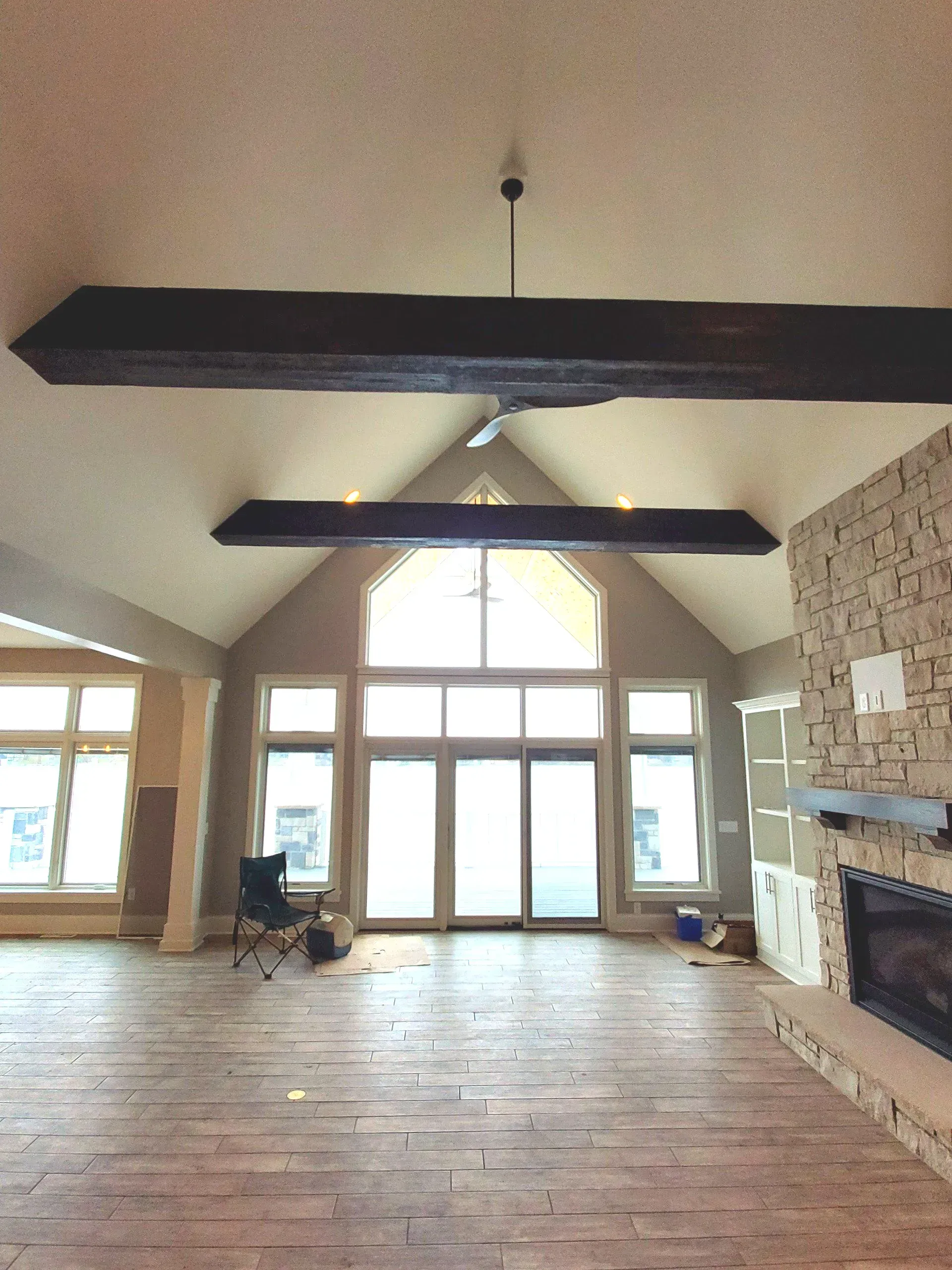 Empty hall with high ceilings, exposed beams, brick fireplace, and large windows letting in daylight.