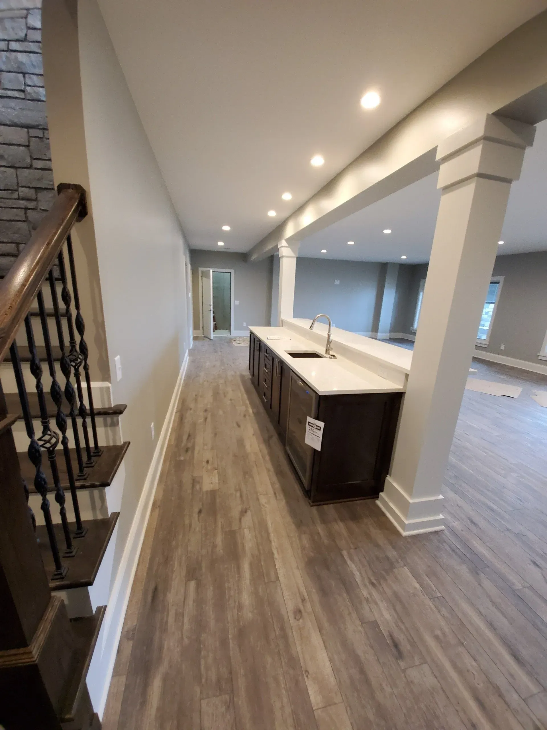 Empty modern kitchen with dark cabinets, white island, wood floors, and recessed lighting in a hallway-like space