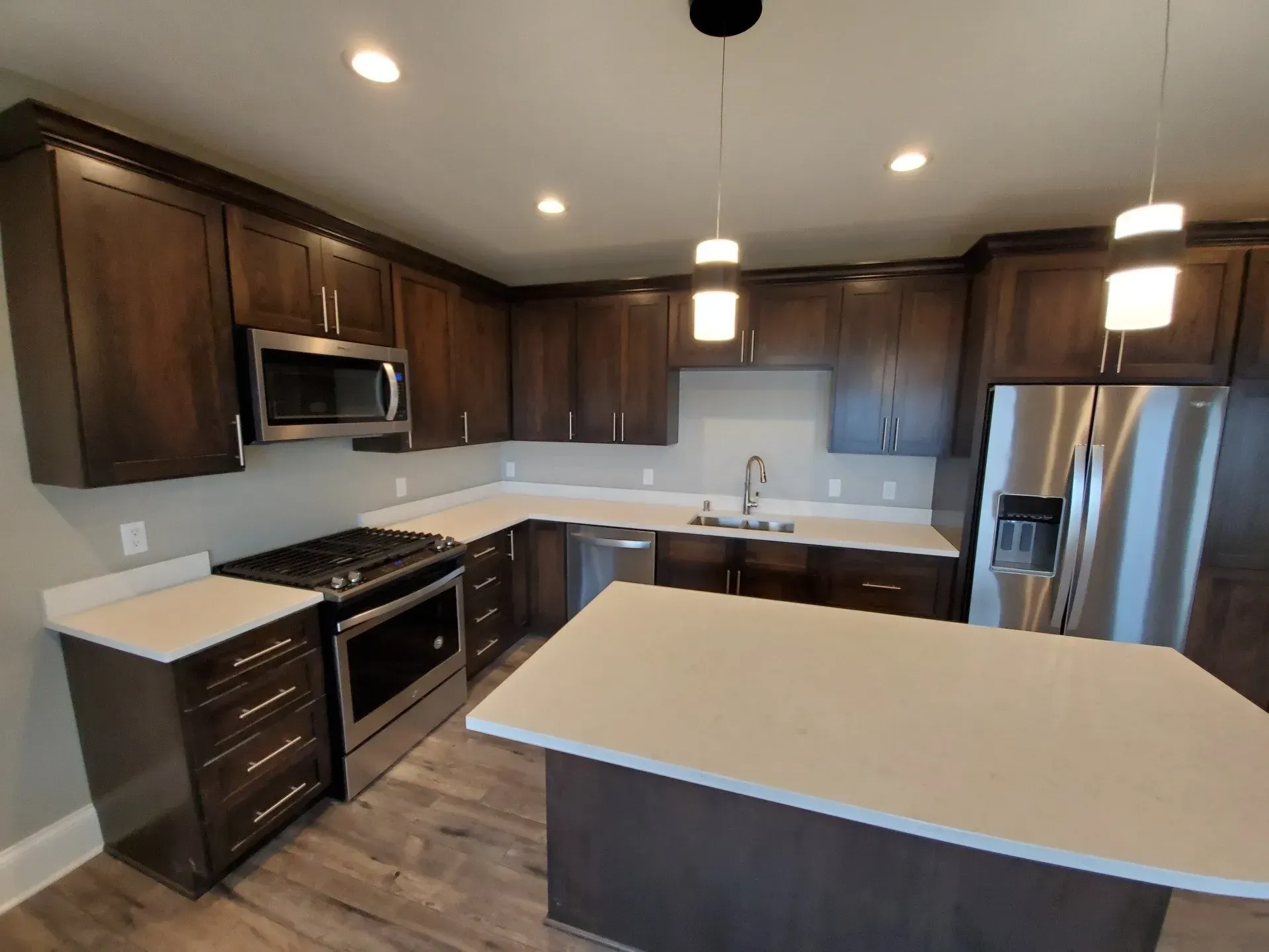Modern kitchen with dark wood cabinets, white countertops, stainless appliances, and a large island