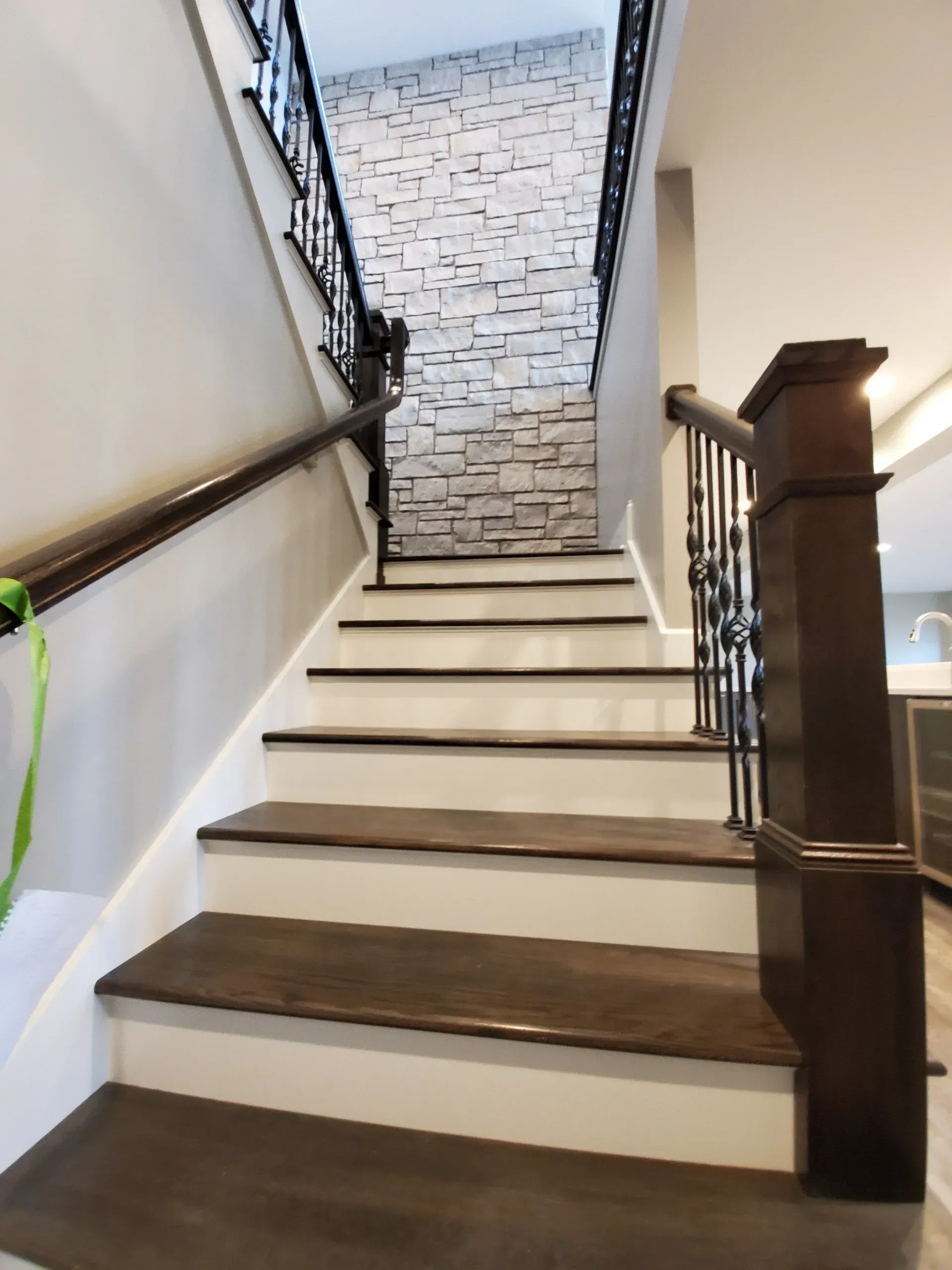 Indoor staircase with dark wood railings, white steps, and a stone accent wall at the top.