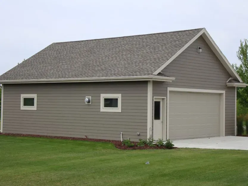 Gray detached garage with a side door and small windows, viewed from a lawn.