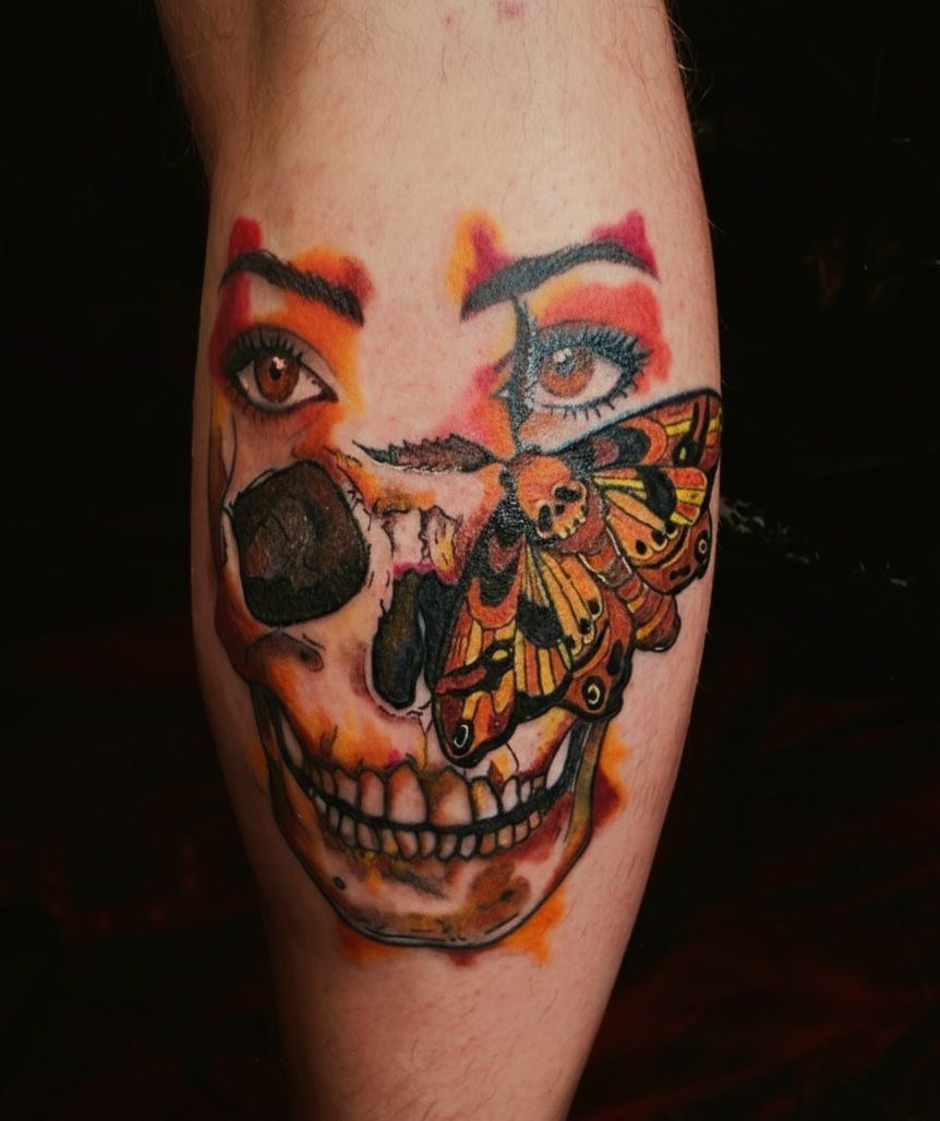 Skull tattoo with moth and woman's eyes, rendered in orange and yellow hues.