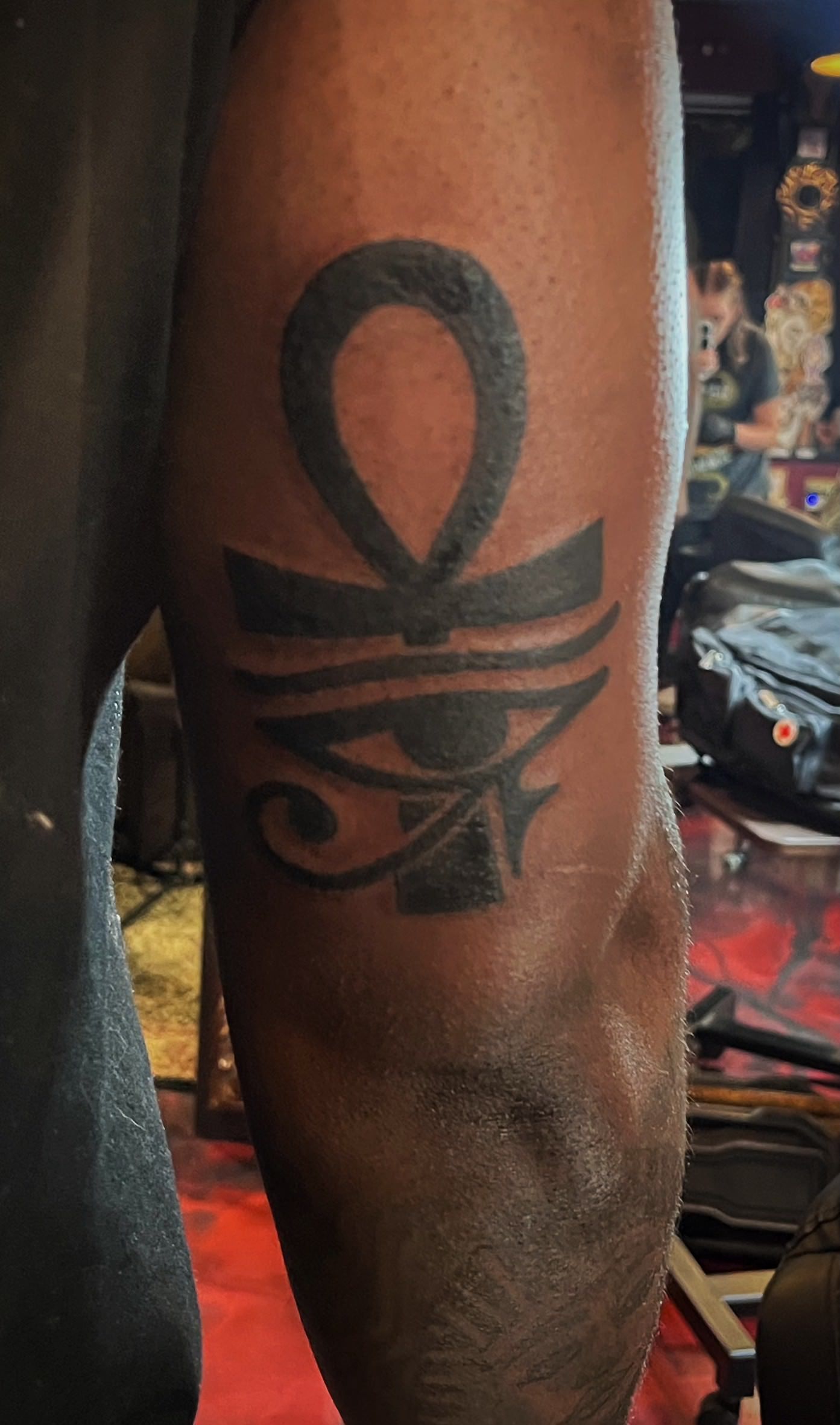 Tattoo of an Ankh and Eye of Horus on an arm. Black ink, visible on dark skin.