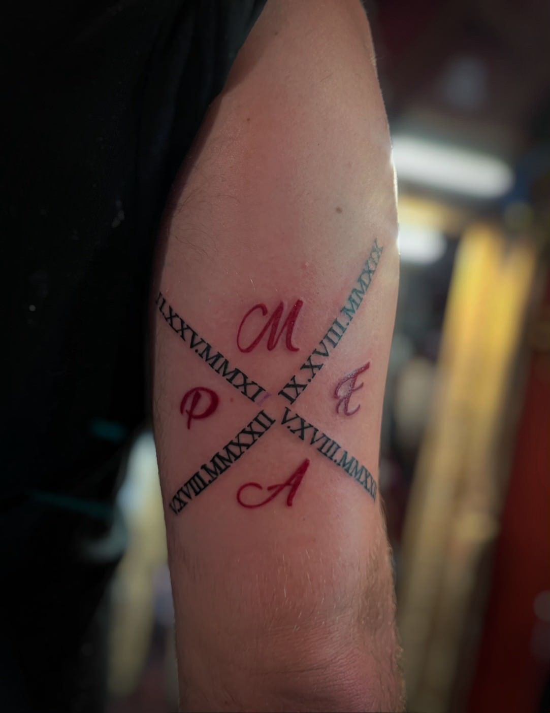 Tattoo of intersecting lines with Roman numerals and letters PMAE in red; forearm.