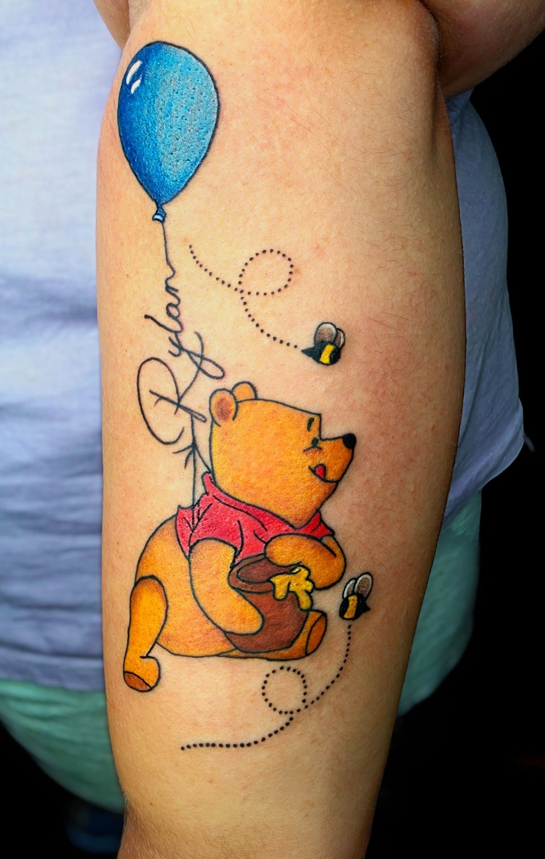 Winnie the Pooh tattoo holding honey, with a blue balloon and bees on arm.