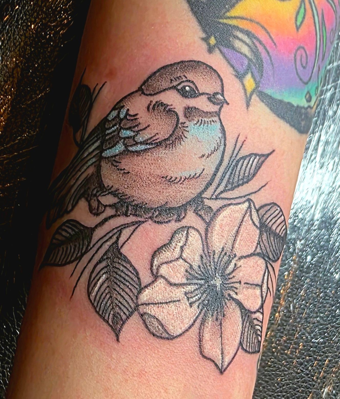 Tattoo of a bird perched on a floral branch, with a large white flower.