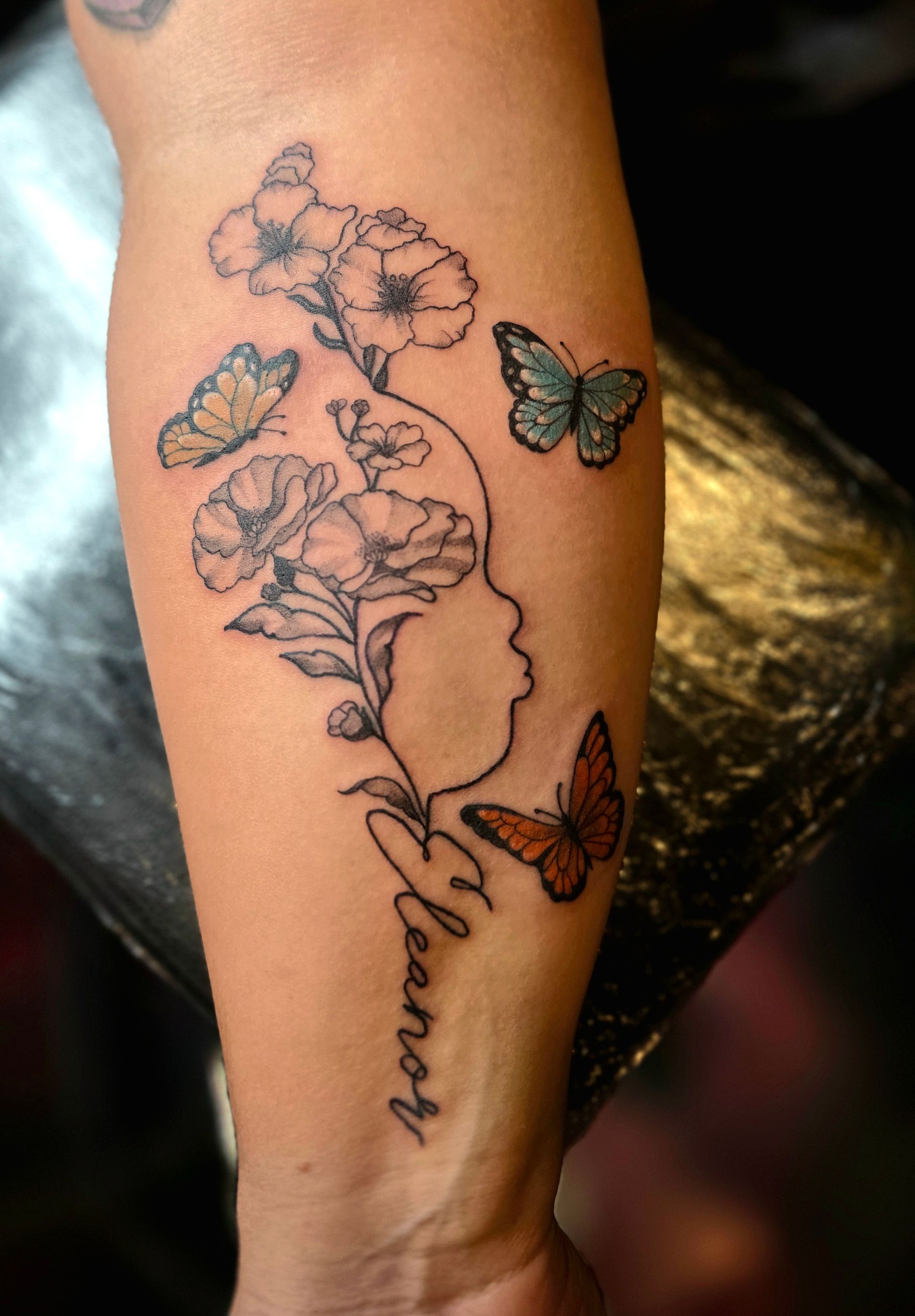 Tattoo on arm: profile with flowers and butterflies, the name 