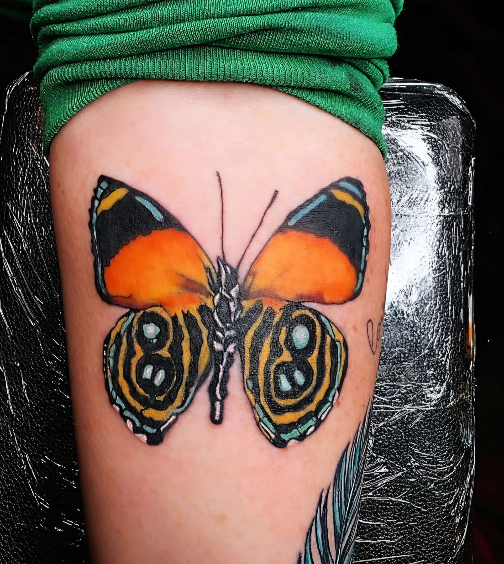 Butterfly tattoo on arm, orange and black with blue details.