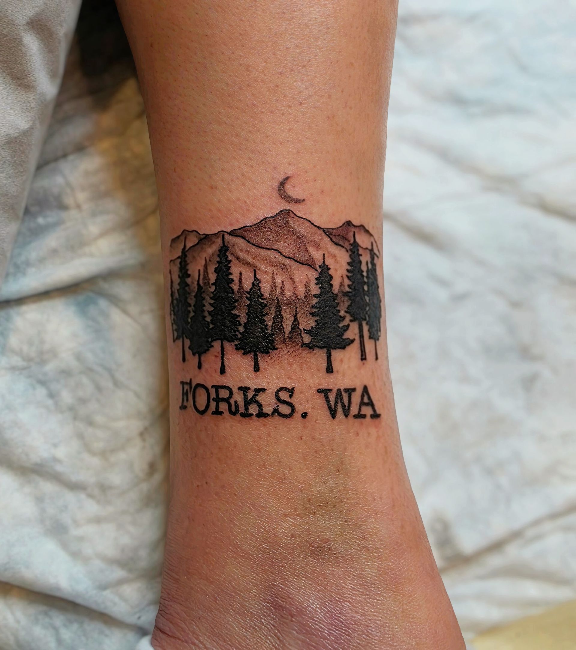 Tattoo of a mountain range, trees, and crescent moon, with 